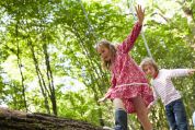 Ein Junge und ein Mädchen spielen im Wald und laufen dabei auf einem Baumstamm Ein Junge und ein Mädchen spielen im Wald und laufen dabei auf einem Baumstamm